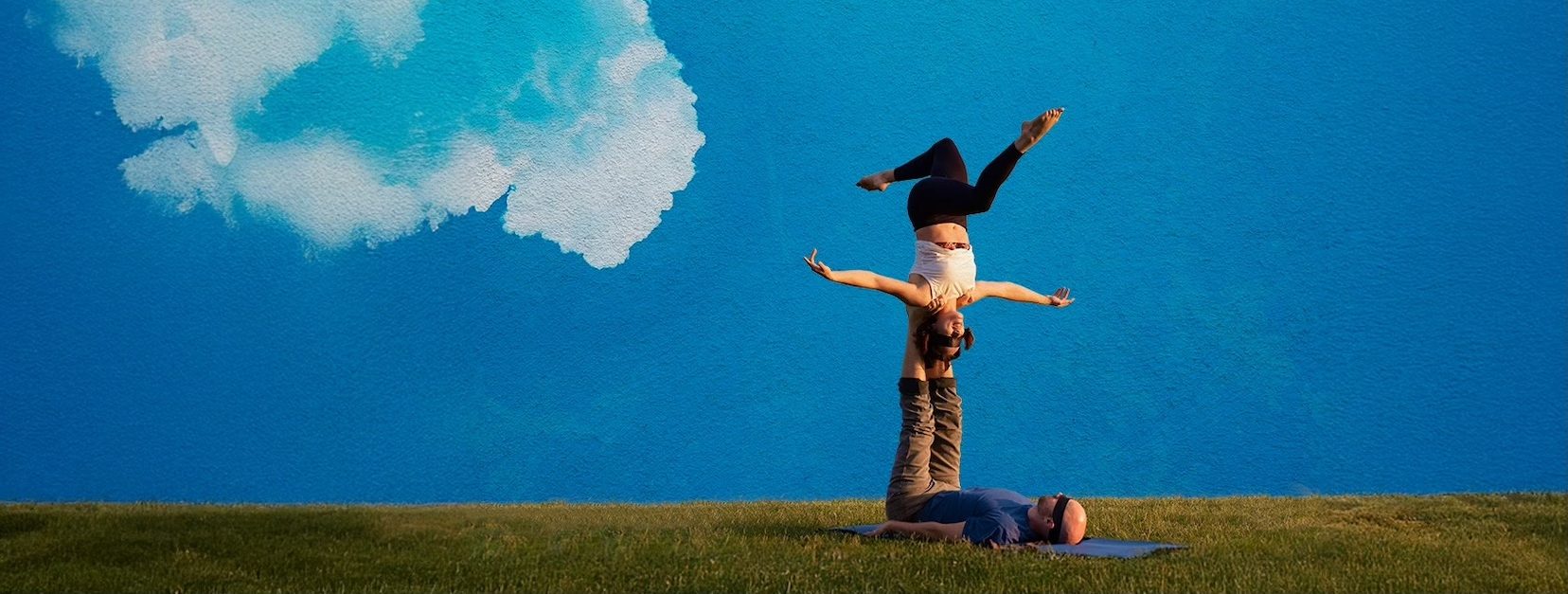 Touching The Sky Movie Poster features two people doing acro on green grass with a blue cloudy sky backdrop